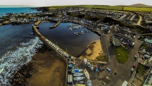 An aerial view of a coastal town with a marina, residential buildings, and a curved harbor.