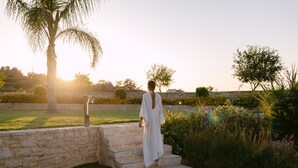 Una donna con un abito bianco sale dei gradini in pietra in un giardino con una palma e fiori.