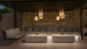 Una moderna zona relax all'aperto con parete in pietra a fondo, lampade a sospensione e una poltrona a dondolo.