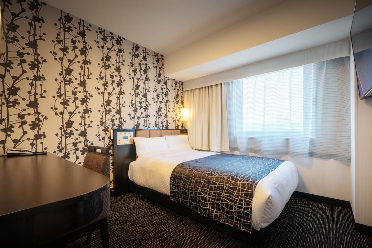 Habitación de hotel con cama, escritorio y pared con estampado floral.