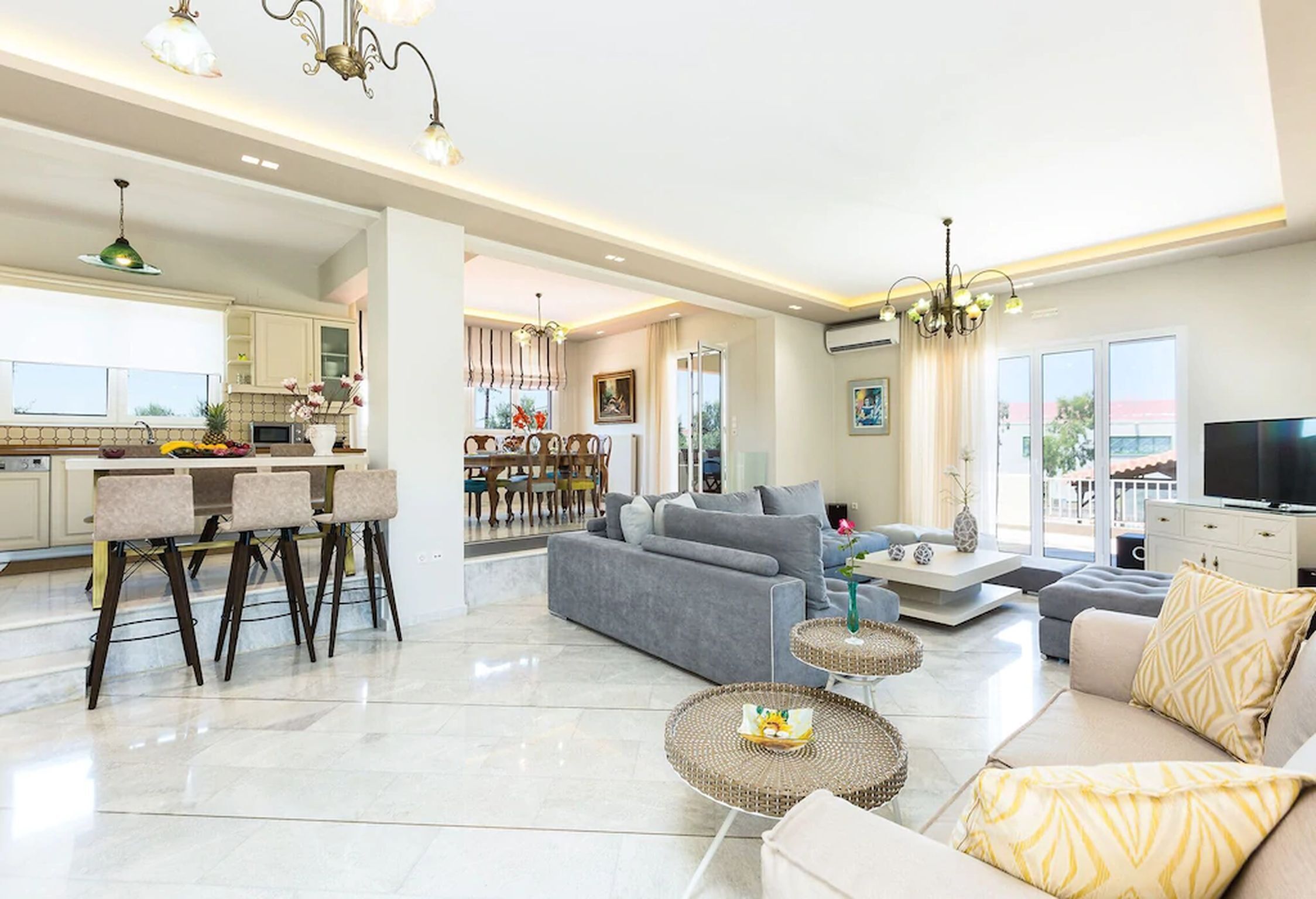 A spacious living area with a grey sofa, a dining table with chairs, and a kitchen in the background.