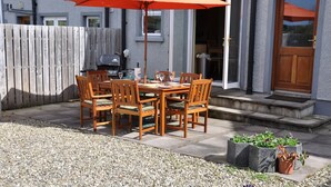 An outdoor patio with a wooden table and chairs, an orange umbrella, and a barbecue grill. - Larchfield, at the centre of the unique North Antrim Coast (Bushmills)