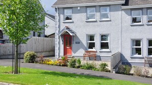 A two-story house with a red door, a wooden bench outside, and a well-maintained garden. - Larchfield, at the centre of the unique North Antrim Coast (Bushmills)