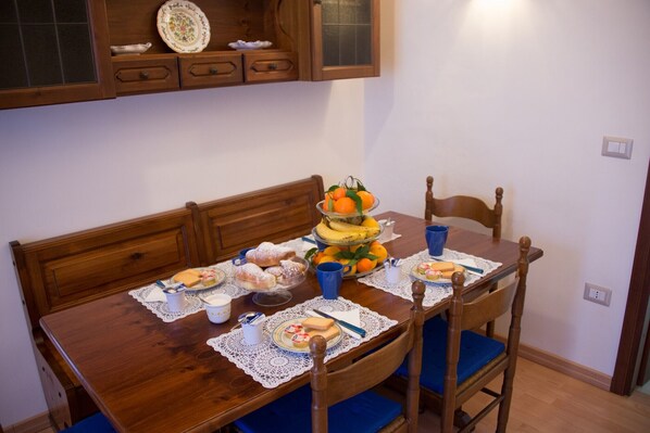 A wooden dining table with a three-tiered fruit stand, blue cups, and various food items.
