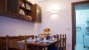 A dining area with a wooden table, blue cushioned chairs, and a buffet with fruits and pastries.