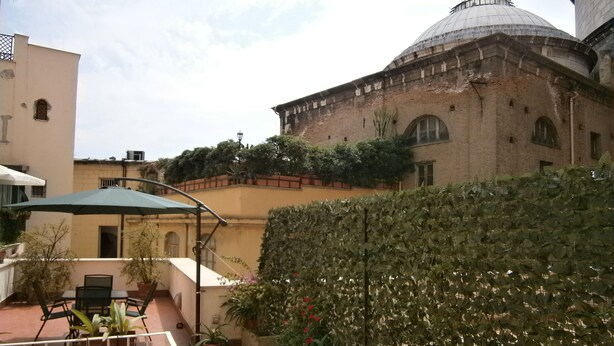 A courtyard with potted plants, outdoor furniture, and a building with a dome.