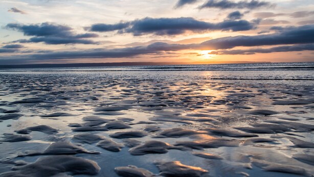 A beach with a sunset, calm water, and a distant shoreline.