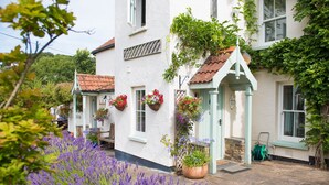 A white building with a tiled roof, a small porch, and hanging flower baskets.