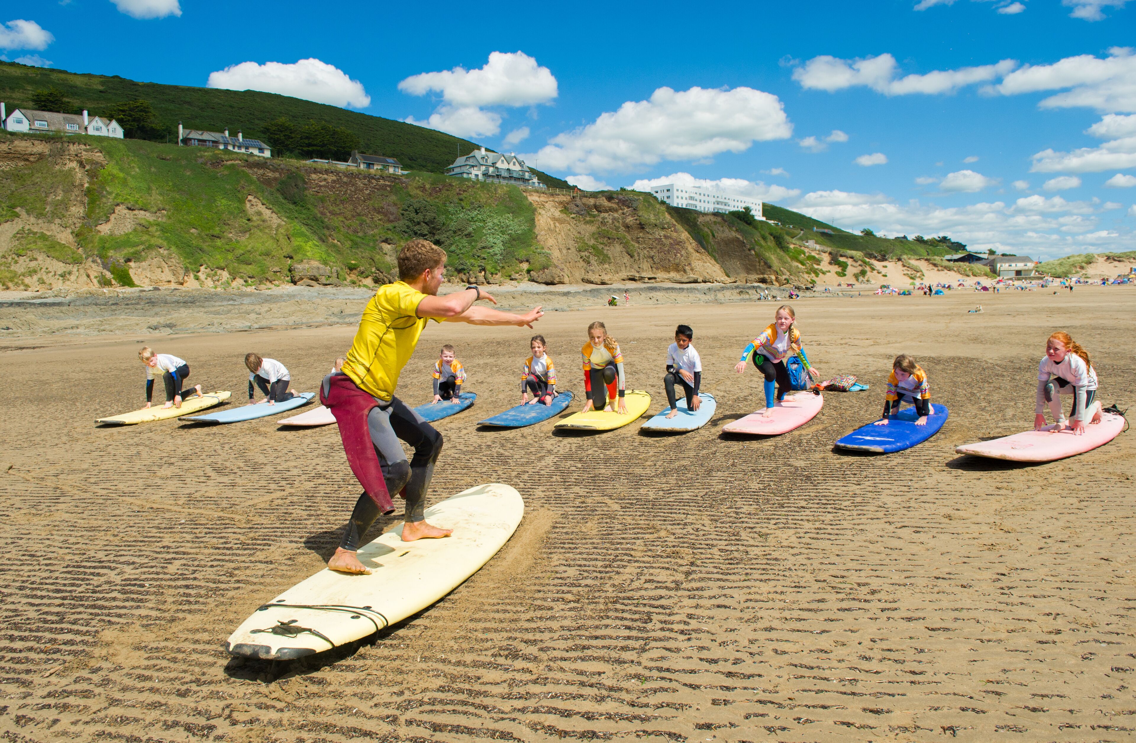 A group of people on surfboards on a sandy beach with houses in the background.