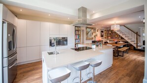 A modern kitchen with white cabinetry, a central island with bar stools, a built-in oven, and a stainless steel refrigerator.
