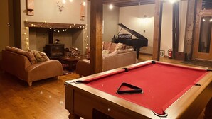 A cozy living room with a pool table, a sofa, a grand piano, and a fireplace.