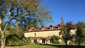 A stone building with a tiled roof, surrounded by a grassy lawn and trees.