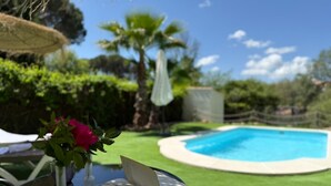 Una piscina rodeada de un césped cuidado, un libro y un vaso sobre una mesa.