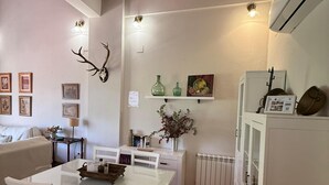 Un comedor con una mesa y sillas blancas, un estante fijado a la pared con objetos decorativos, y un radiador.
