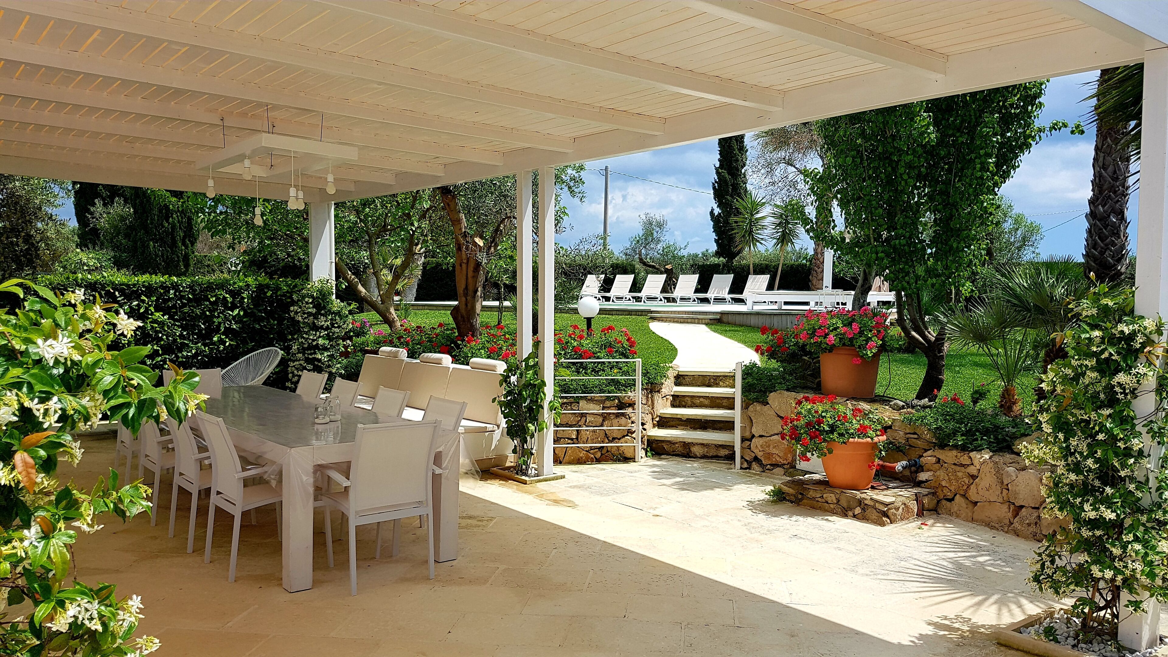 An outdoor patio with a covered seating area, a stone wall, and a view of a pool and lounge chairs.