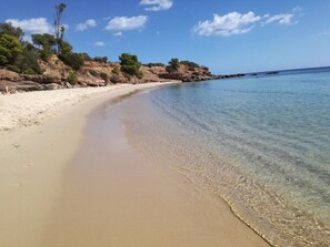 Une plage de sable fin bordée d’une eau claire, parsemée de rochers et dotée d’une végétation clairsemée.