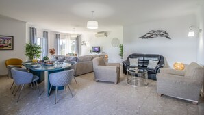 Una sala de estar moderna con comedor, que incluye un sofá, sillones, una mesa de centro y un televisor.