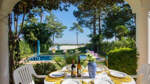 Un área de comedor al aire libre con vista a una piscina y follaje.
