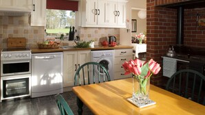 Una cocina con armarios blancos, una mesa de madera y un jarrón con flores.