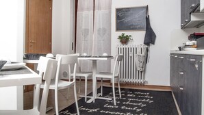 A compact kitchen with white chairs, a dining table, a blackboard with writing, and a potted plant. - CityWalls Guest House Bergamo (Bergamo)