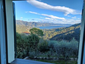 A view from a window overlooking a coastal landscape with mountains, a body of water, and a town in the distance.
