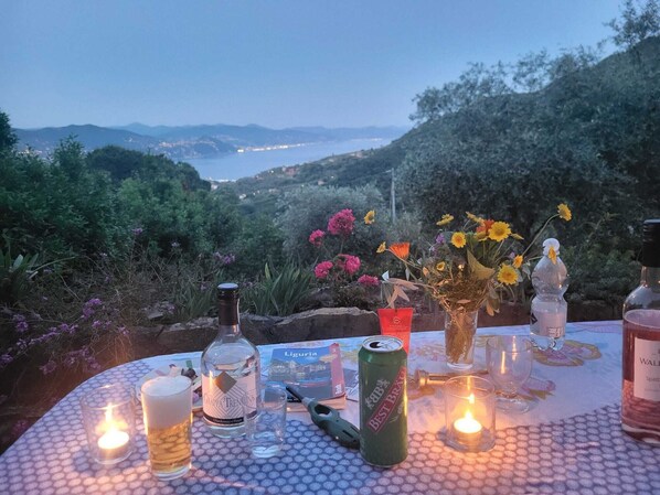 A table set outdoors with a scenic view, featuring a bottle, a can, candles, and a glass.