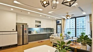 Un appartement moderne comprenant une cuisine, un coin repas et un salon. Il est doté d’une grande fenêtre, d’un ventilateur de plafond et d’un réfrigérateur.