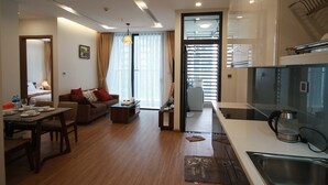 Une chambre d’hôtel moderne comprenant un coin repas, un salon avec un canapé et une table basse, une cuisine équipée d’un évier et d’une bouilloire, ainsi qu’une grande fenêtre avec des rideaux.