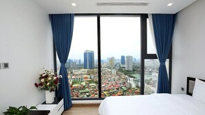 Une chambre moderne avec un grand lit, une vue sur le paysage urbain et une plante en pot.