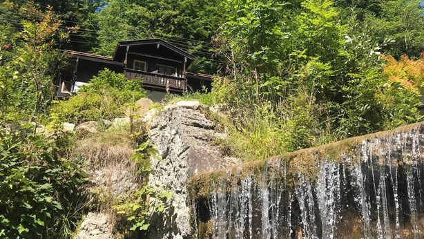 Uma cabana com varanda com vista para uma cascata, rodeada por uma floresta densa.