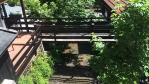 Uma ponte de madeira sobre um pequeno riacho, com um caminho de pedra que leva a um edifício com telhado de cerâmica.