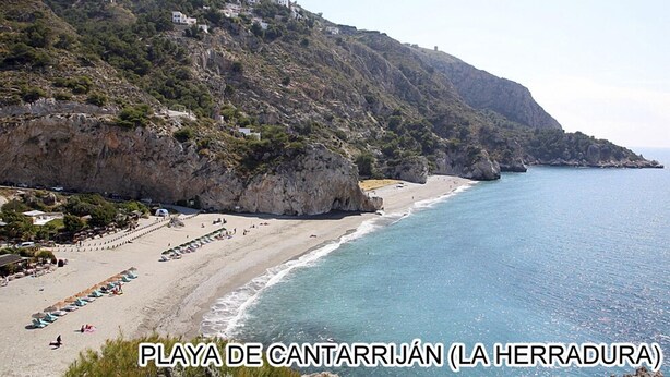 Un paisaje costero con una playa, acantilados rocosos y edificios en la ladera.