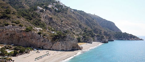 A coastal landscape with a beach, rocky cliffs, and buildings on the hillside.