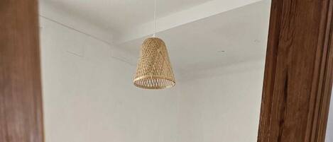 A bedroom with a wooden bed, a bedside table with a lamp, and a woven ceiling light fixture.