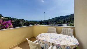 A balcony with a table and chairs, overlooking a scenic landscape with hills and a road.