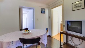 A dining area with a round table, chairs, a TV on a stand, and a door leading to another room.