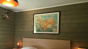 A room with a bed, two bedside tables, a framed map on the wall, and a small table with a candle.