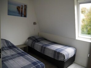 A small, simple room with two single beds, a small table, and a window.