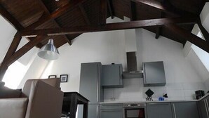 Une cuisine avec un plafond haut et des poutres apparentes en bois, des meubles de couleur grise et un four encastré.