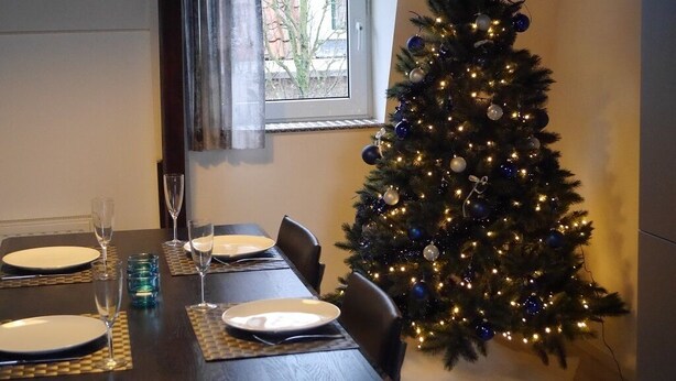 Une table à manger dressée avec des assiettes, des verres et un sapin de Noël illuminé.