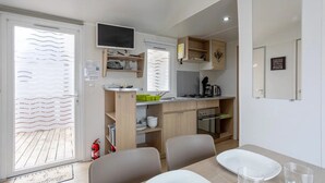 A compact kitchen with a dining area, a TV mounted above the counter, and a small seating arrangement. - Mobil-Homes Deux Chambres (Saint-Jean-de-Monts)