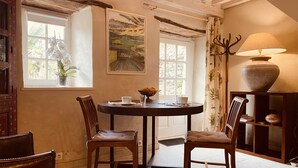 Uma área de refeições com uma mesa redonda, duas cadeiras, um vaso com flores e um quadro na parede.