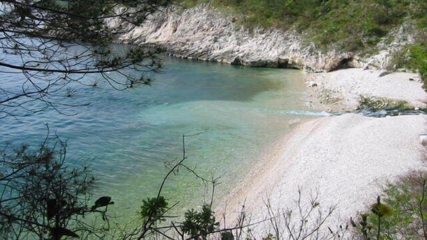 Un paisaje costero con una playa despejada, acantilados rocosos y abundante vegetación.