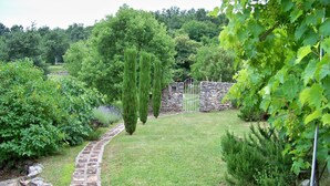 Un sendero de piedra conduce a un muro de piedra con una puerta, rodeado de exuberante vegetación y un césped bien cuidado.
