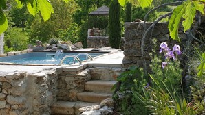 Una piscina de piedra con cascada, rodeada de exuberante vegetación y una escalera de piedra.