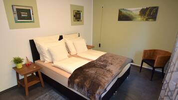 A bedroom with a bed, a chair, a nightstand, and a wall-mounted picture.