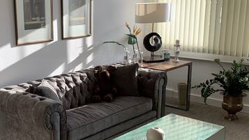 Un salon avec un canapé gris, une table basse en verre, des œuvres d’art encadrées accrochées au mur, une lampe et une plante en pot.