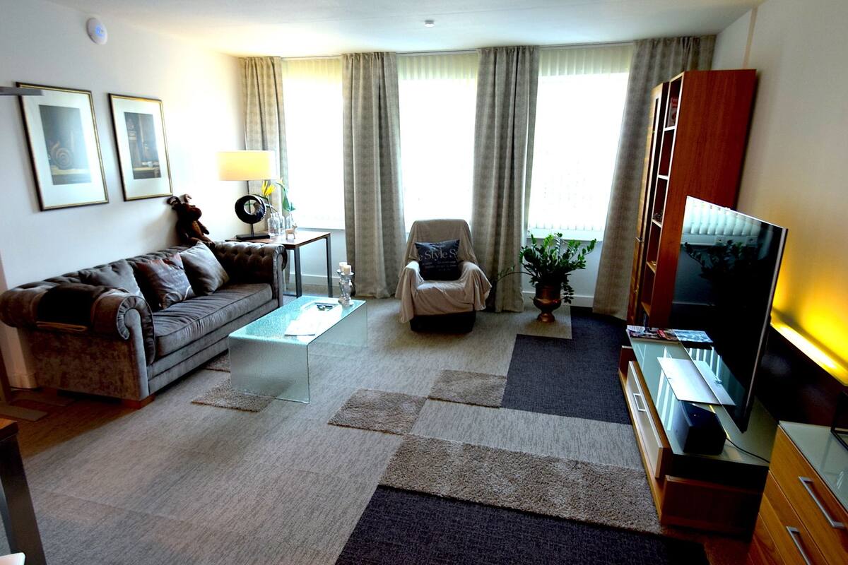 A living room with a sofa, armchair, coffee table, TV, and a potted plant.