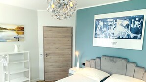 Un dormitorio moderno con puerta de madera, cama con ropa de cama blanca y toallas azules, un estante blanco y un cuadro de Picasso en la pared.