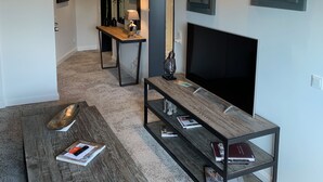 Una sala de estar moderna con una mesa de centro de madera oscura, una mesita auxiliar de cristal y un televisor de pantalla plana.